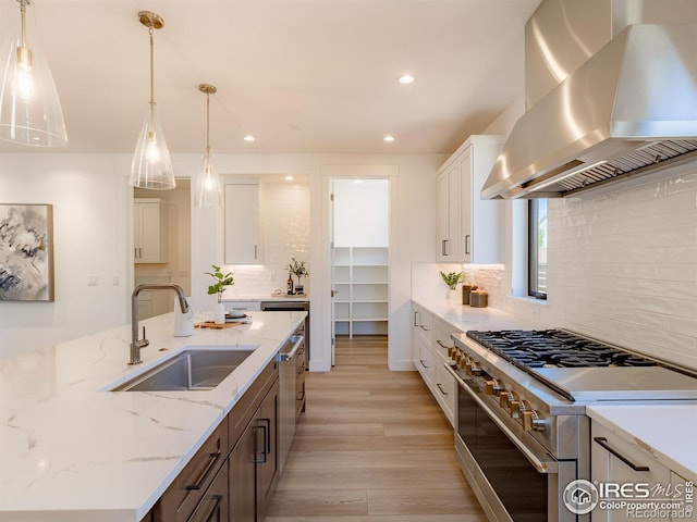 kitchen featuring tasteful backsplash, wall chimney range hood, appliances with stainless steel finishes, sink, and white cabinets