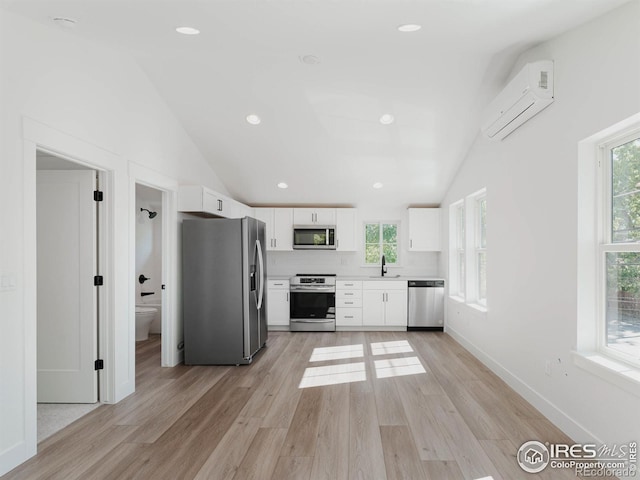 kitchen with a healthy amount of sunlight, an AC wall unit, stainless steel appliances, and white cabinetry