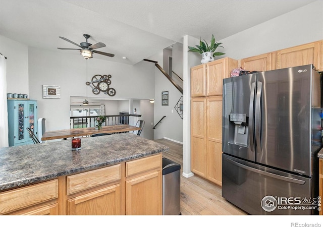 kitchen featuring stainless steel refrigerator with ice dispenser, dark stone counters, light wood-type flooring, light brown cabinetry, and ceiling fan