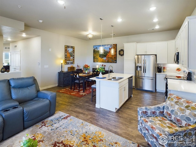 kitchen featuring dark wood-type flooring, stainless steel appliances, a center island with sink, sink, and white cabinetry