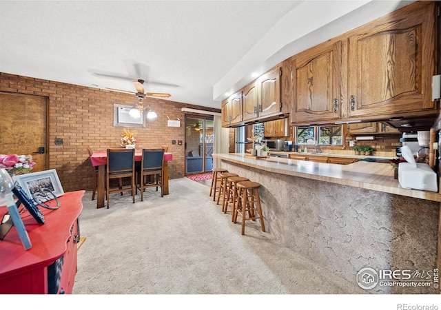 kitchen featuring brick wall, plenty of natural light, light colored carpet, and ceiling fan