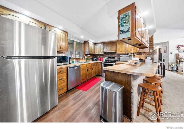 kitchen with hardwood / wood-style flooring, a breakfast bar area, stainless steel appliances, backsplash, and sink