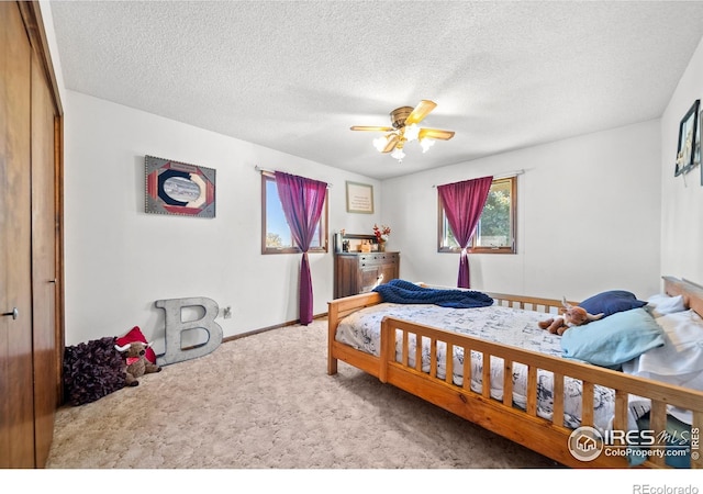 bedroom featuring a textured ceiling, light colored carpet, a closet, and ceiling fan