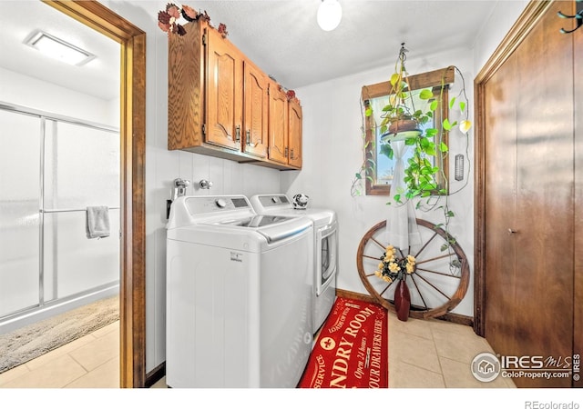 laundry area with independent washer and dryer, a textured ceiling, cabinets, and light tile patterned floors