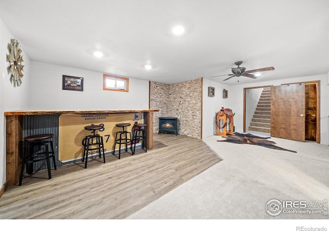 interior space featuring light hardwood / wood-style flooring, indoor bar, a wood stove, and ceiling fan