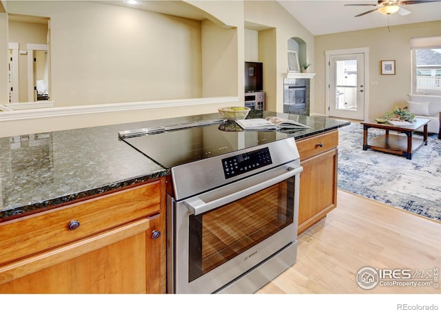 kitchen featuring lofted ceiling, stainless steel range with electric cooktop, a tiled fireplace, ceiling fan, and light hardwood / wood-style flooring