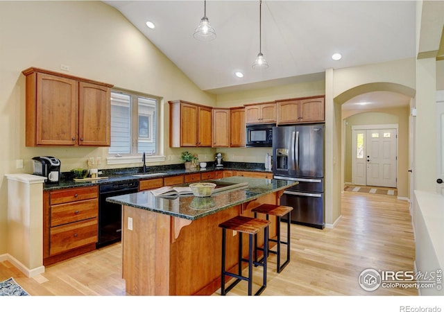 kitchen featuring dark stone countertops, black appliances, light hardwood / wood-style floors, and a kitchen island