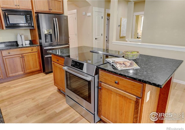 kitchen featuring stainless steel appliances, a kitchen island, light hardwood / wood-style floors, and dark stone counters