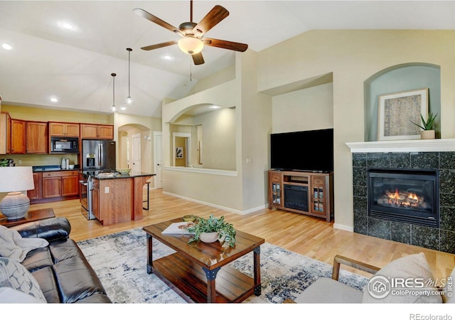 living room featuring a tile fireplace, lofted ceiling, ceiling fan, and light hardwood / wood-style floors