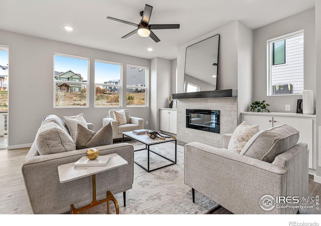 living room featuring a fireplace, a healthy amount of sunlight, light wood-type flooring, and ceiling fan