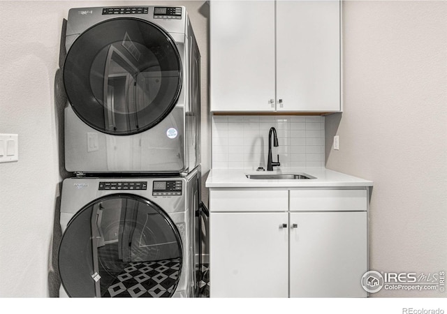 washroom with stacked washer / drying machine, cabinets, and sink