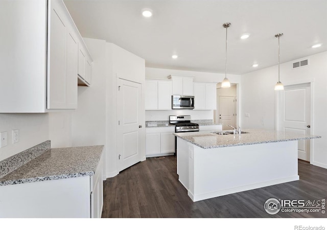 kitchen with dark hardwood / wood-style floors, stainless steel appliances, a center island with sink, pendant lighting, and white cabinets