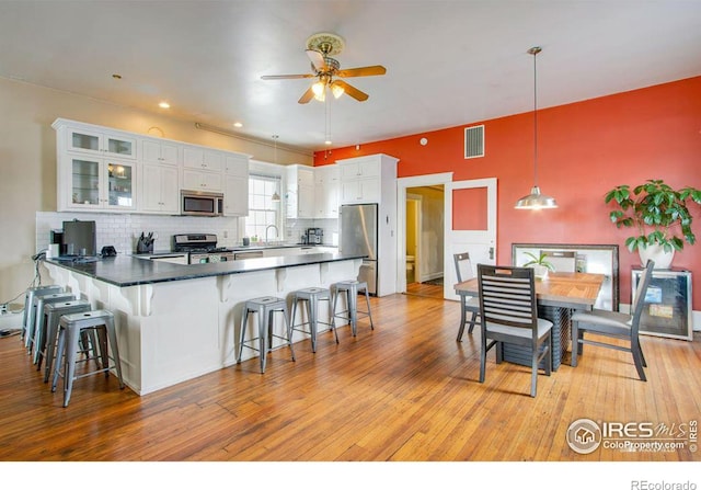 kitchen with decorative light fixtures, light wood-type flooring, stainless steel appliances, and white cabinetry