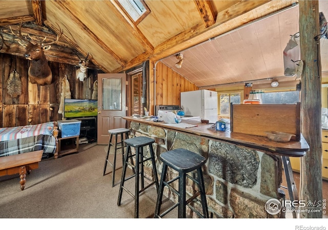 kitchen featuring light carpet, white fridge, wood walls, and vaulted ceiling with skylight