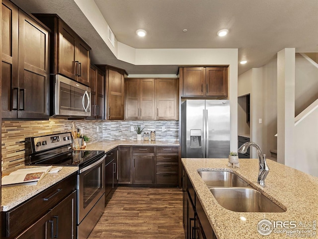 kitchen featuring stainless steel appliances, sink, dark hardwood / wood-style flooring, light stone counters, and tasteful backsplash