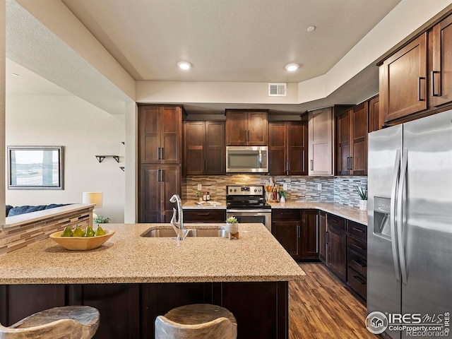 kitchen with a kitchen breakfast bar, sink, appliances with stainless steel finishes, light stone counters, and dark hardwood / wood-style flooring