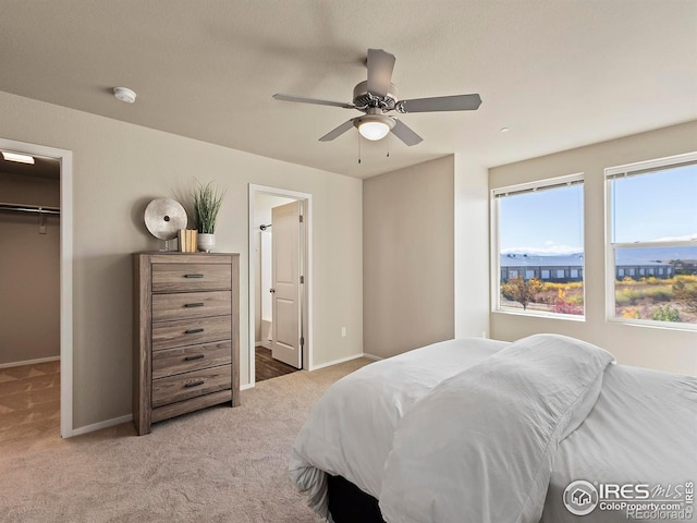 bedroom with a closet, light carpet, a spacious closet, ensuite bathroom, and ceiling fan