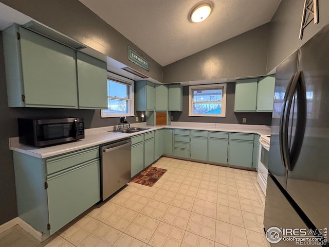 kitchen featuring lofted ceiling, sink, green cabinetry, stainless steel appliances, and a textured ceiling