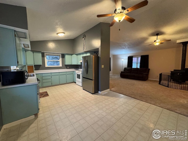 kitchen featuring electric stove, stainless steel refrigerator, light carpet, vaulted ceiling, and a wood stove