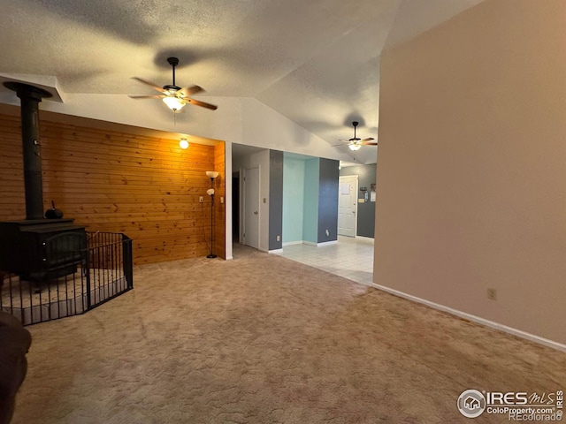 unfurnished living room featuring lofted ceiling, light colored carpet, a wood stove, and wooden walls