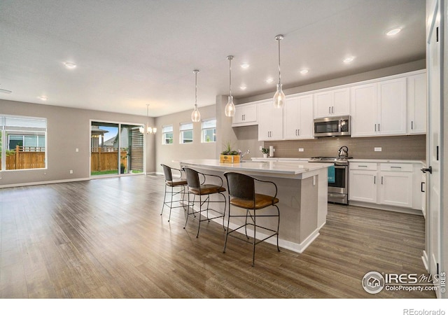 kitchen with dark hardwood / wood-style floors, a center island with sink, white cabinets, pendant lighting, and appliances with stainless steel finishes