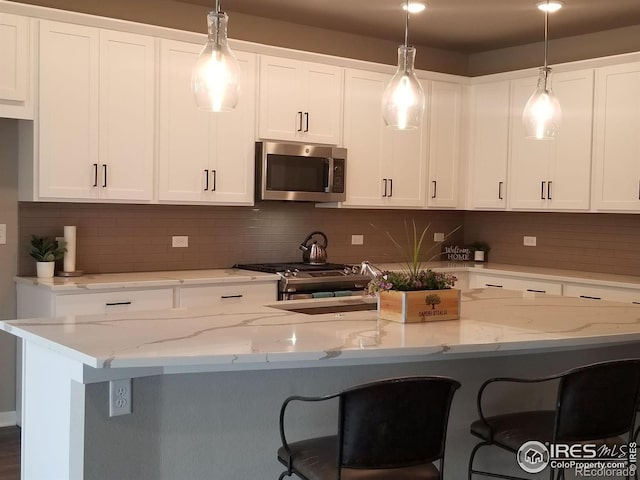 kitchen featuring backsplash, hanging light fixtures, white cabinetry, stainless steel appliances, and light stone counters