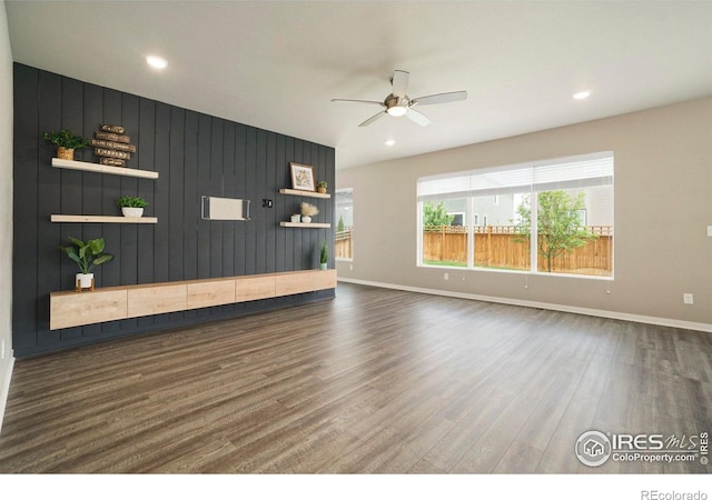 unfurnished living room featuring ceiling fan, dark hardwood / wood-style flooring, and wooden walls