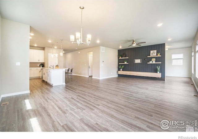 unfurnished living room with sink, light wood-type flooring, and ceiling fan with notable chandelier