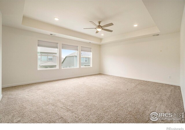 carpeted spare room with ceiling fan and a raised ceiling