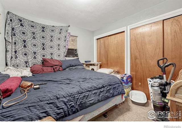 carpeted bedroom featuring a textured ceiling, cooling unit, and two closets