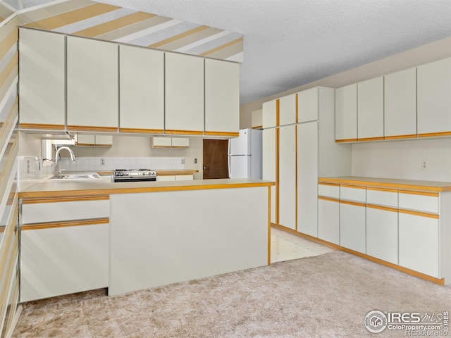 kitchen with white cabinetry, stainless steel gas range oven, sink, and white refrigerator