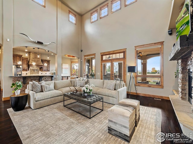 living room with french doors, a stone fireplace, hardwood / wood-style flooring, and a towering ceiling