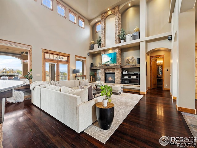 living room with a towering ceiling, dark hardwood / wood-style floors, a stone fireplace, and a wealth of natural light