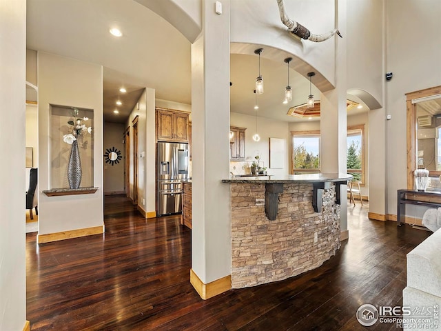 interior space with kitchen peninsula, stainless steel fridge, decorative light fixtures, a breakfast bar, and dark hardwood / wood-style floors