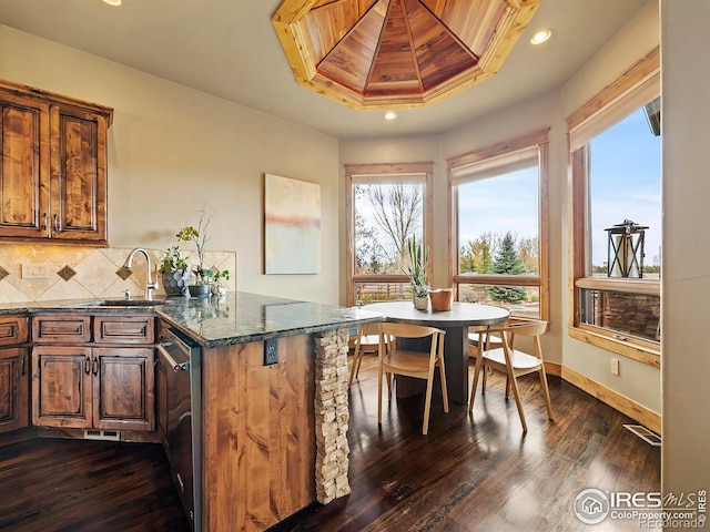 kitchen with dark hardwood / wood-style floors, a tray ceiling, dark stone counters, and backsplash