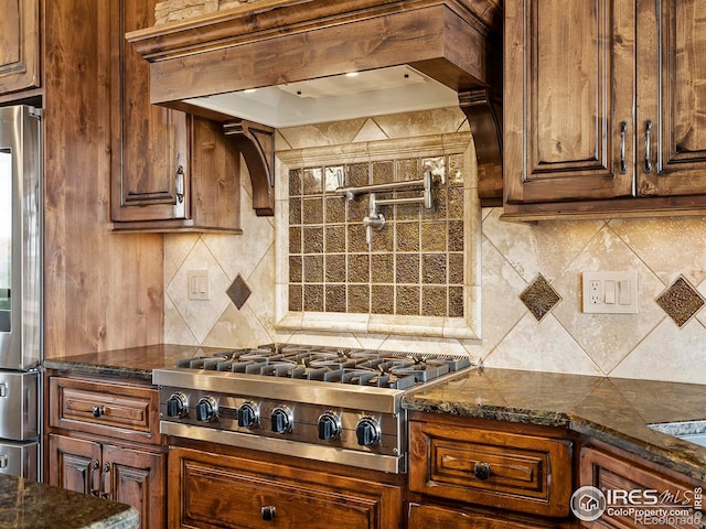 kitchen with custom range hood, stainless steel appliances, decorative backsplash, and dark stone counters