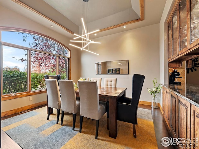 dining area featuring a tray ceiling, a chandelier, and dark wood-type flooring