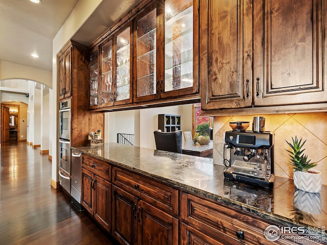 kitchen with double oven, tasteful backsplash, dark hardwood / wood-style floors, and dark stone countertops