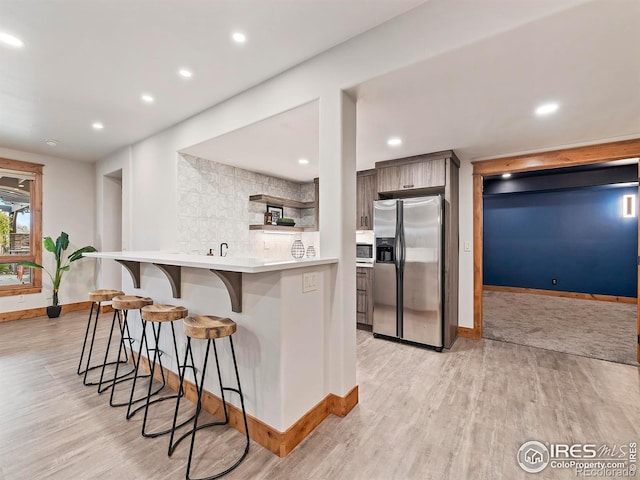 kitchen featuring a kitchen breakfast bar, light hardwood / wood-style flooring, kitchen peninsula, and stainless steel appliances