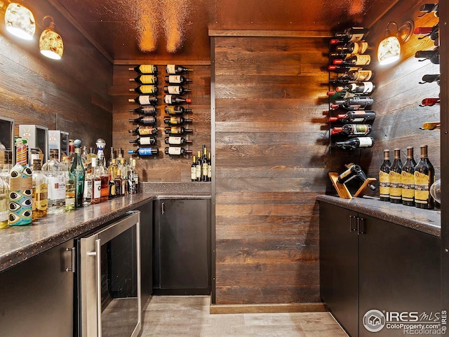 wine room with wood walls, light wood-type flooring, and beverage cooler