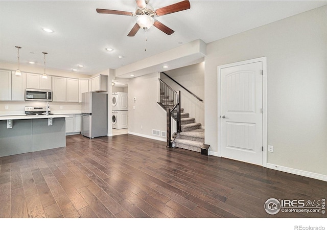 kitchen with stacked washer and clothes dryer, dark hardwood / wood-style flooring, pendant lighting, stainless steel appliances, and white cabinets