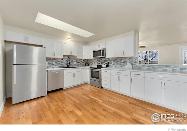 kitchen with backsplash, sink, white cabinetry, appliances with stainless steel finishes, and light hardwood / wood-style floors