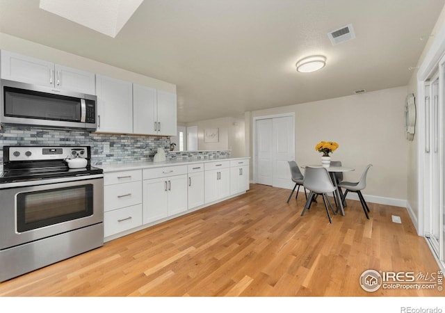 kitchen with appliances with stainless steel finishes, tasteful backsplash, white cabinetry, and light hardwood / wood-style floors