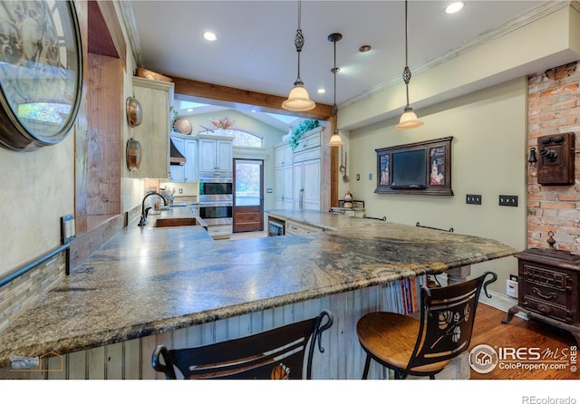 kitchen with dark hardwood / wood-style floors, a breakfast bar area, kitchen peninsula, sink, and decorative light fixtures