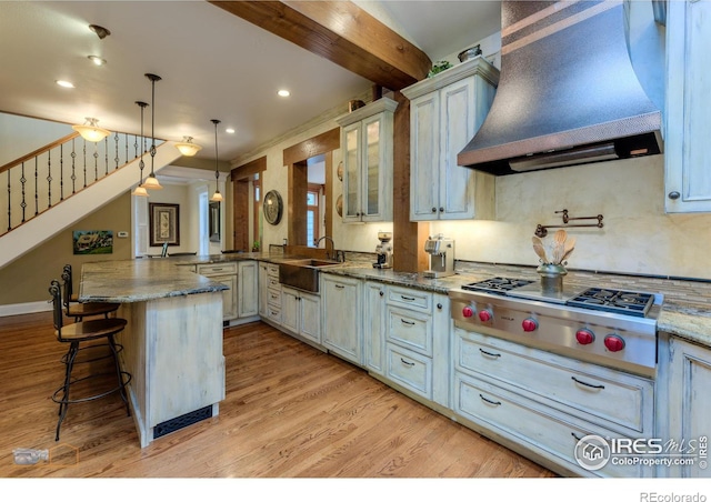 kitchen featuring custom exhaust hood, kitchen peninsula, a breakfast bar area, light hardwood / wood-style floors, and decorative light fixtures