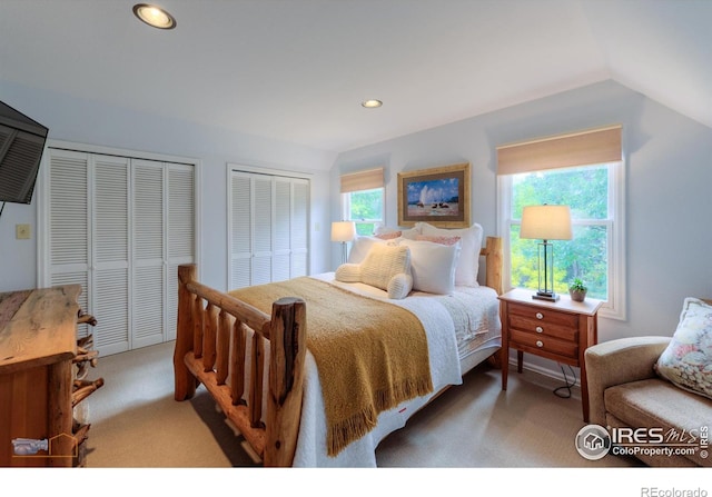 bedroom with multiple closets, lofted ceiling, and light colored carpet