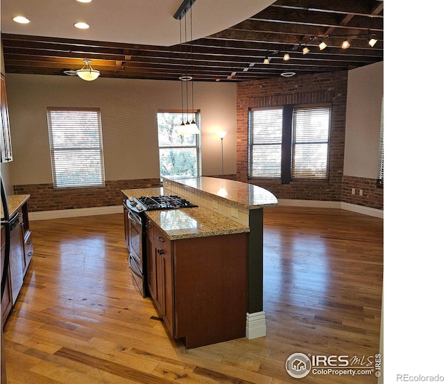 kitchen featuring hanging light fixtures, light stone countertops, light hardwood / wood-style flooring, brick wall, and stainless steel gas range