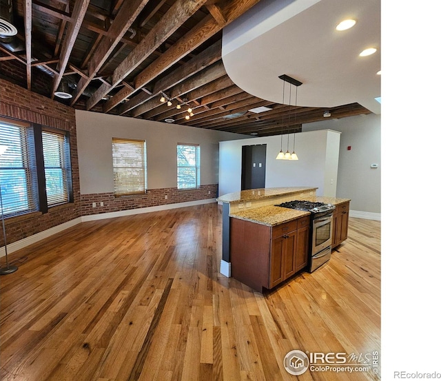 kitchen with stainless steel gas stove, brick wall, light stone countertops, pendant lighting, and light wood-type flooring