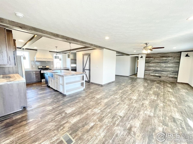 kitchen featuring a center island with sink, stainless steel range oven, wooden walls, premium range hood, and dark hardwood / wood-style floors