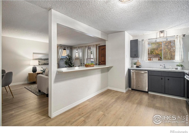 kitchen with a textured ceiling, stainless steel dishwasher, sink, and light wood-type flooring